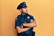 Handsome hispanic man wearing police uniform looking to the side with arms crossed convinced and confident