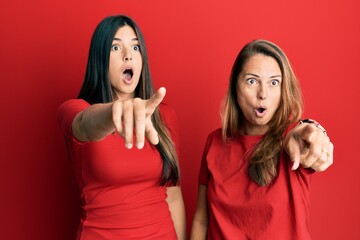 Poster - Hispanic family of mother and daughter wearing casual clothes over red background pointing with finger surprised ahead, open mouth amazed expression, something on the front