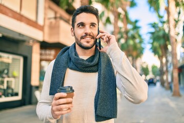 Young hispanic man smiling happy talking on the smartphone and drinking take away coffee at the city.