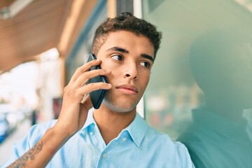 Wall Mural - Young latin man with serious expression talking on the smartphone at the city.