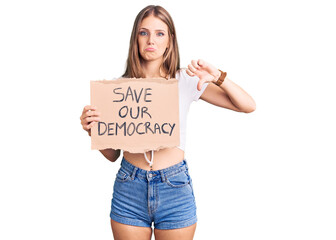 Wall Mural - Young beautiful blonde woman holding save our democracy protest banner with angry face, negative sign showing dislike with thumbs down, rejection concept