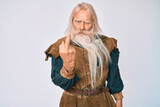Old senior man with grey hair and long beard wearing viking traditional costume showing middle finger, impolite and rude fuck off expression