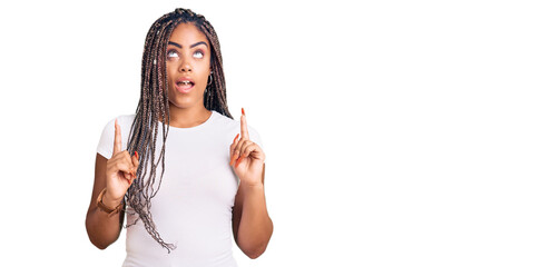 Sticker - Young african american woman with braids wearing casual clothes amazed and surprised looking up and pointing with fingers and raised arms.