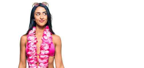 Beautiful hispanic woman wearing bikini and hawaiian lei smiling looking to the side and staring away thinking.