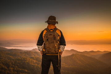 Wall Mural - young man hiker on a top of a mountain standing on top of cliff in summer mountains at sunset and en