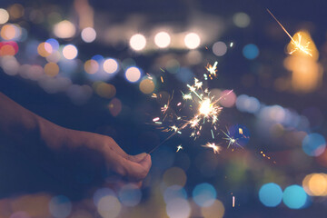 Female hands holding sparkler on bokeh background. Glittering burning sparkler for celebration christmas,festival party background