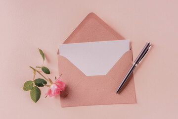 Invitation or greeting card mock up in a kraft envelope, overhead flat lay shot on a pink pastel background, toned image