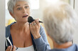 © goodluz - Senior woman with short grey hair putting make-up on