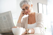 © goodluz - Portrait of smiling mature woman at home reading newspaper