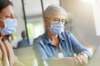 © goodluz - Business women working in office with face mask during 2019-ncov pandemia