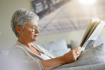 Wall Mural - Senior woman reading newspaper, relaxed in sofa