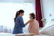 © Newman Studio - Home Caregiver Comforting Senior Woman Patient Sitting in Her Bedroom. Nurse Putting Her Hand Over Elderly Patient Shoulder in Hospital Room.