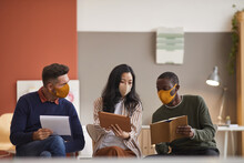 Multi-ethnic Group Of Three Business People Wearing Face Masks While Discussing Project In Office