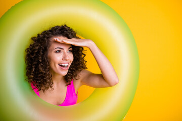 Photo portrait of young girl looking in distance hand at forehead inside inflatable green ring wearing fuchsia swim wear isolated on vivid yellow colored background