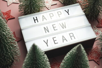 Wall Mural - Happy New Year word in light box with Christmas tree top view on pink background