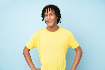 Young african american man isolated on blue background posing with arms at hip and smiling