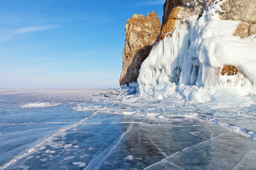 Beautiful landscape of frozen lake Baikal on a Sunny day in February. Blue ice with cracks and hummocks near the icy rocks of Olkhon island. Winter holidays, ice travel. Natural background