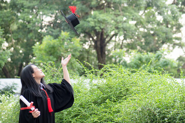 Asian student with college or university degree throwing her academic hat up in commencement ceremony day