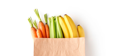 Paper grocery bag full of healthy fruits and vegetables - banana, carrots and celery, top view isolated on white background