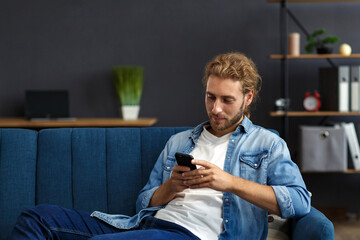 Curvy guy using smartphone and smiling. Happy man using mobile phone apps, texting message, browsing internet, looking at smartphone, sitting at home. Young people working with mobile devices.