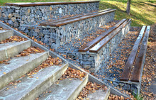Grandstand In The Park By A Concrete Staircase Made Of Gabion Baskets With Gray Stones Arranged Inside. The Seating Areas Of The Benches Are Steps Made Of Planks.