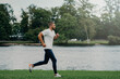 © VK Studio - Athlete bearded man runs along beautiful landscape, demonstrates endurance, dressed in active wear, goes jogging near river, breathes fresh air. Sport, exercising, fitness and workout concept