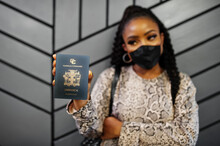 African American Woman Wearing Black Face Mask Show Jamaica Passport In Hand. Coronavirus In America Country, Border Closure And Quarantine, Virus Outbreak Concept.