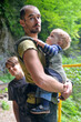 © Kirill - Travel with small children. Father with baby in carrier and ten year old son walking in mountain gorge.