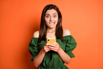 Wall Mural - Photo of stressed woman hold telephone bite mouth wear dark shirt isolated on orange color background