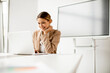 © BGStock72 - Young woman working on laptop in bright office with big screen behind her