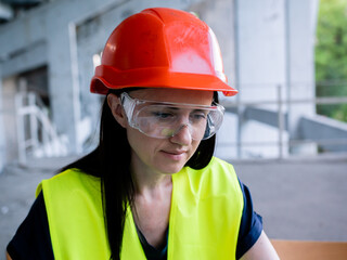 Woman architect in protective helmet and goggles working on personal computer on new project at construction site