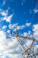Metal Power Pole Structure With Powerlines In Sunlight Against Cloudy Blue Sky