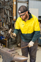 A Tradesman Wearing High Vis Clothing Hammering A Steel Rod On An Anvil.