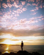 Man Standing On The Edge Of A Rockpool Infront Of A Dramatic Sunrise