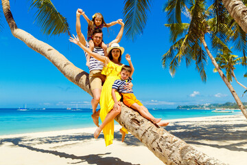 Young happy family-mom, dad, daughter and son having fun on a coconut tree on a sandy tropical beach. The concept of travel and family holidays.