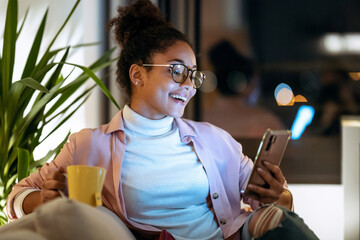 Wall Mural - Happiness young entrepreneur woman using her smart phone while drinking a cup of coffee sitting on couch in the office.