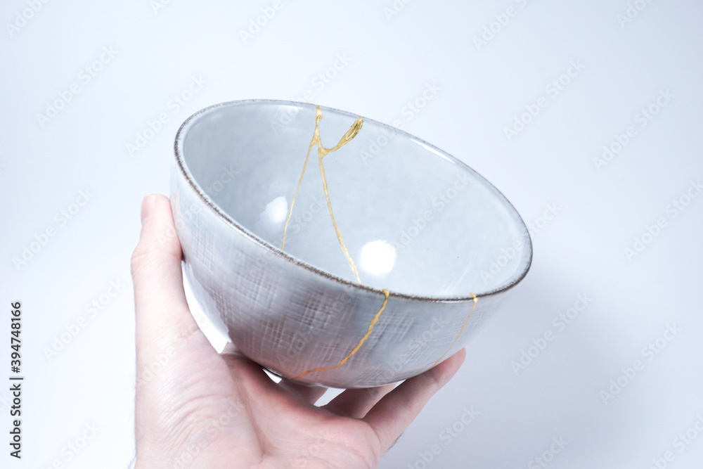 Hand holding kintsugi bowl. Gold cracks restoration on pottery restored ...