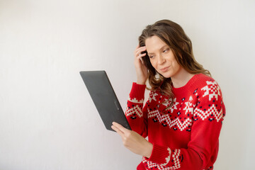 Young caucasian woman in a new year christmas sweater  isolated on white background looking into a tablet buying gifts online