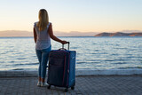 Fototapeta Tęcza - young blond woman with suitcase and the view of sea, small island and mainland from thasos island greece
