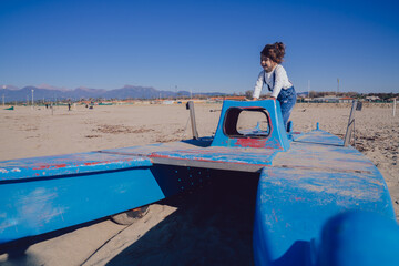 little girl while playing on a blue boat on the winter beach