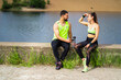 © Georgii - Athletic young couple in stylish sportswear having break during workout sitting with phone and bottle of water outdoor