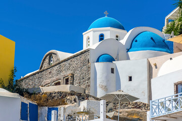 Wall Mural - Blue church domes dominate the skyline in the village of Oia, Santorini in summertime