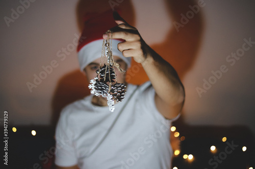 Cuadros en Lienzo Person in a white T-shirt and a Christmas hat on his head shows decorations on the Christmas tree