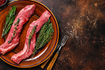 Raw flank beef meat steak on a plate. Dark background. Top view. Copy space