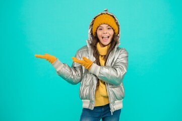 Wall Mural - smiling stylish child presenting product, copy space. autumn season shopping. teenage girl in silver puffer jacket. trendy warm clothing. accessories shop for kid. enjoy weather on christmas holidays