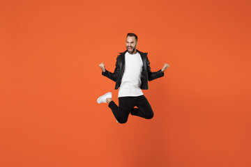 Canvas Print - Full length of happy joyful young bearded man 20s wearing basic white t-shirt black leather jacket jumping doing winner gesture clenching fists isolated on orange colour background studio portrait.