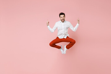 Wall Mural - Full length of crazy screaming young bearded man 20s wearing basic casual white shirt jumping depicting heavy metal rock sign horns up gesture isolated on pastel pink color background studio portrait.