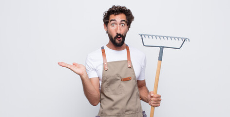 Wall Mural - young man looking surprised and shocked, with jaw dropped holding an object with an open hand on the side