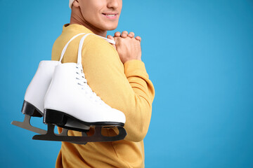 Wall Mural - Happy man with ice skates on light blue background, closeup. Space for text