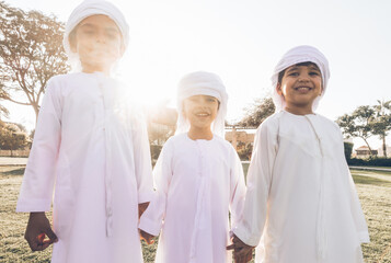 Wall Mural - Children playing together in Dubai in the park. Group of kids wearing traditional kandura white dress from arab emirates